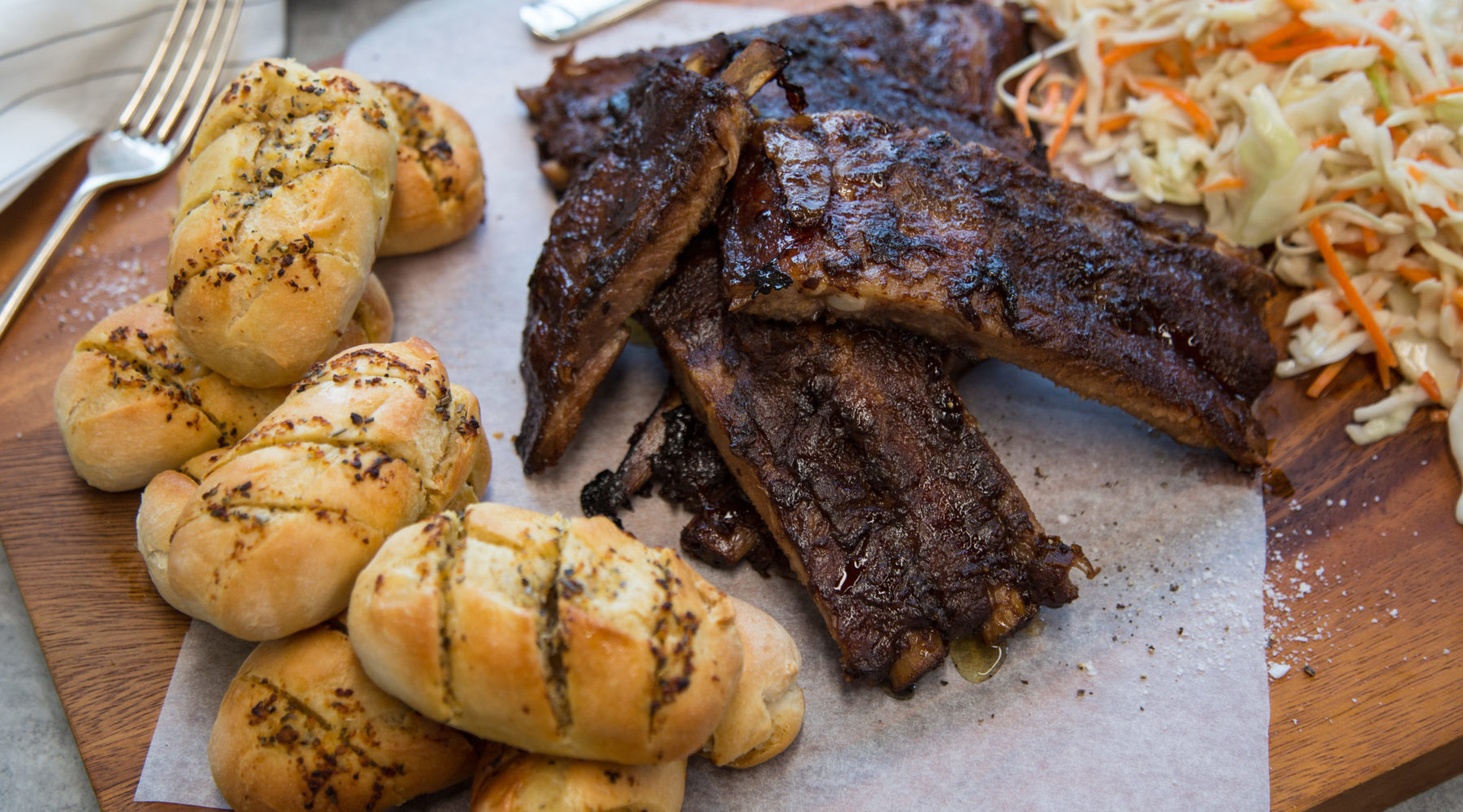 Cooked ribs and mini garlic breads and slaw on a board.