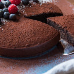 Whole chocolate cake topped with berries, a slice being served out.