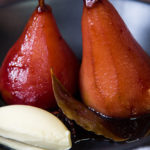 Two whole red poached pears, bay leaf and white cream on a plate.