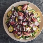 Colourful salad of meat, corn cobs, greens, red heaped on a round plate.