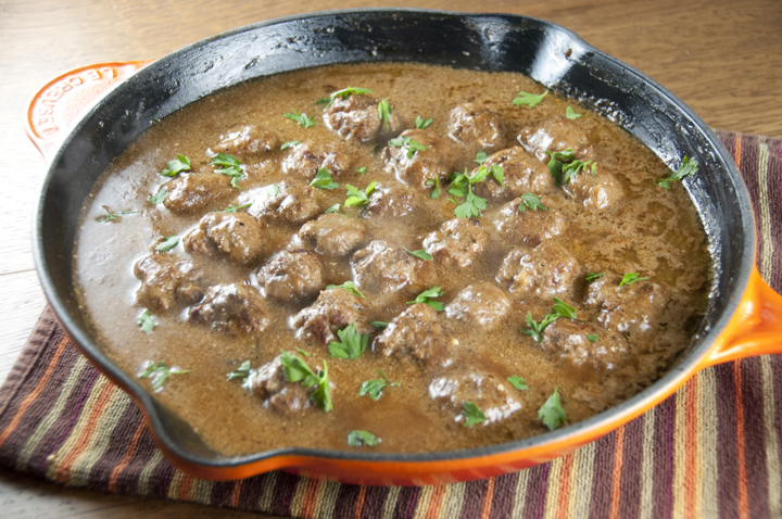 A orange skillet full of creamy sauce meatballs with herbs.