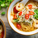 Two bowls of noodle soup woth prawns, sprouts, green and chilli