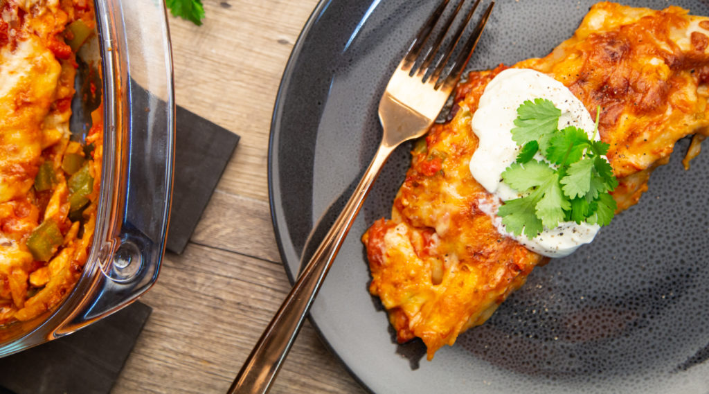 A chicken enchilada with sour cream and coriander on top sitting on a grey plate with a gold fork.