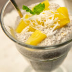 A glass of creamy food topped with pineapple chunks and mint leaves.
