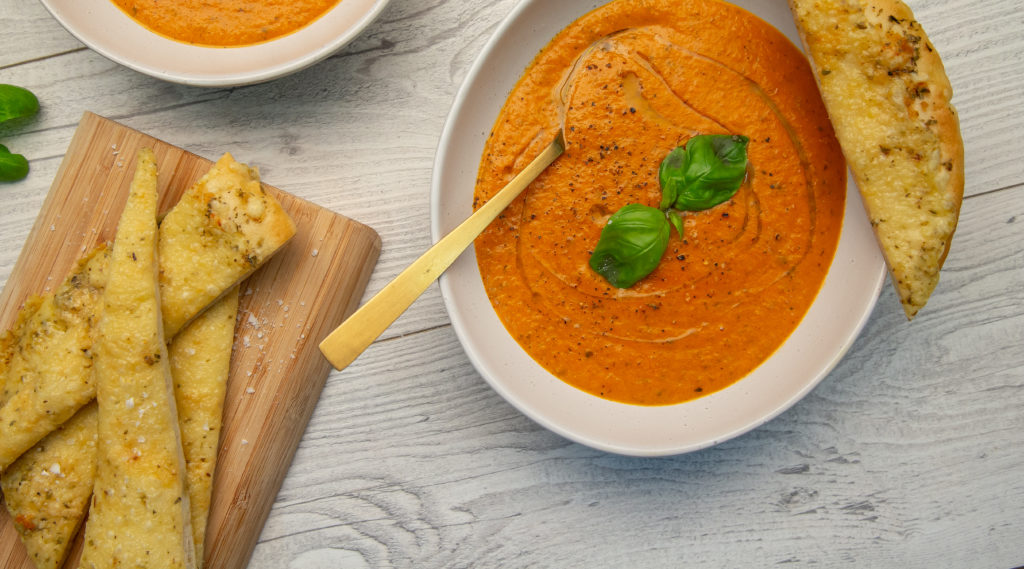 Two bowls of tomato soup topped with herb, and slices of flat bread.