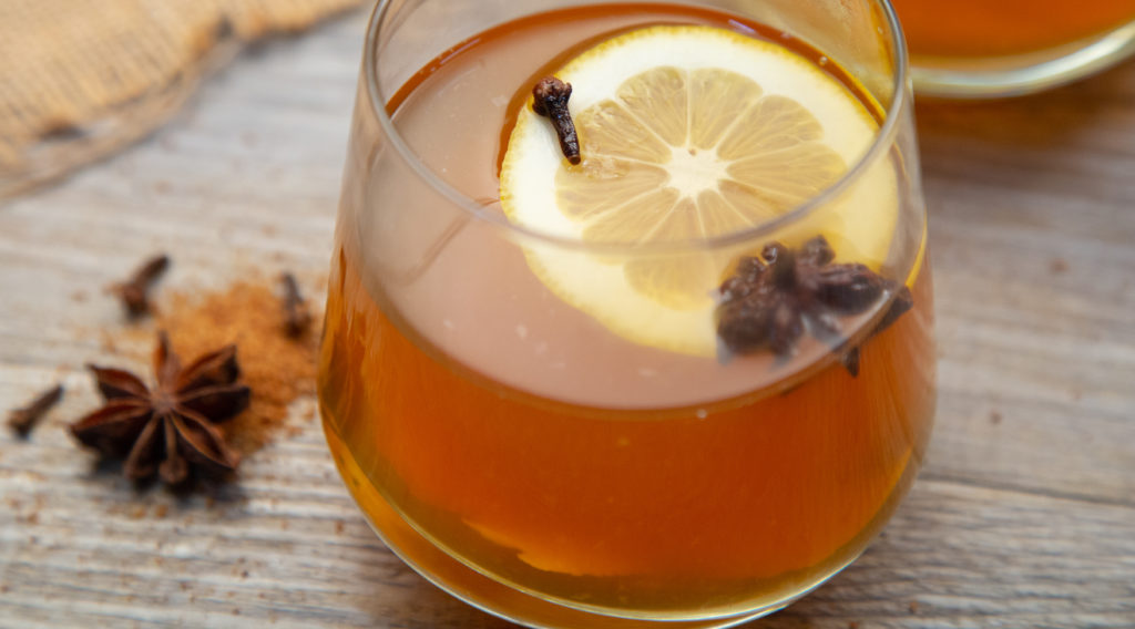 A glass of amber coloured drink with a lemon slice, start anise and a clove in it.