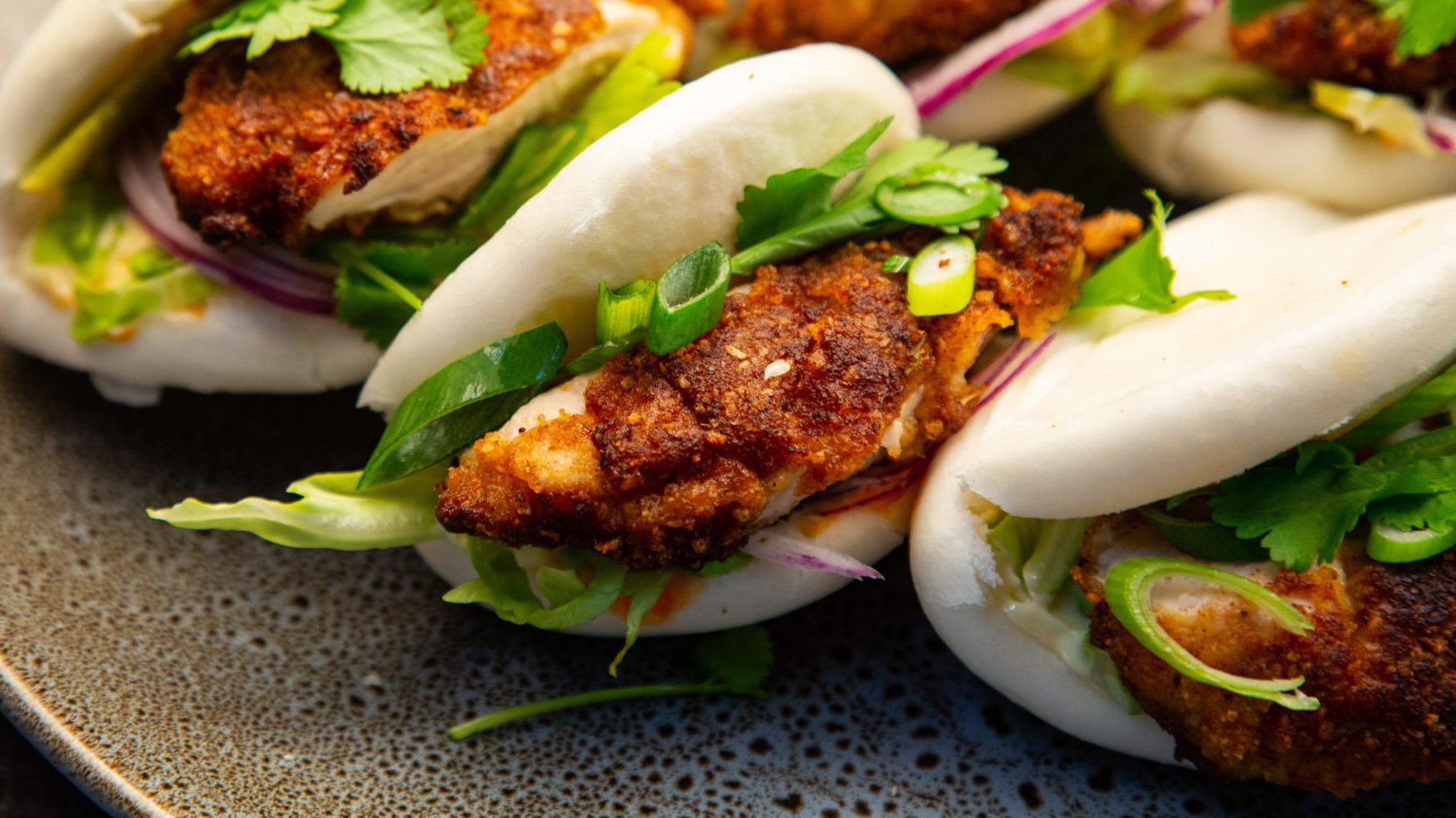 Three fried chicken and salad filled bao buns on a tray