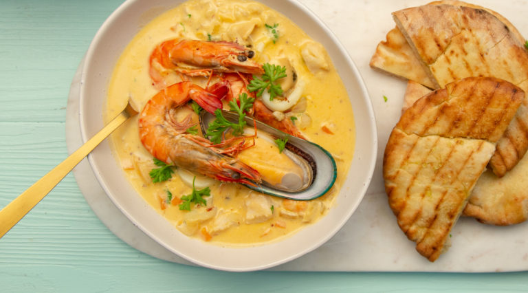 A bowl of seafood chowder with a spoon and toasted pita breads