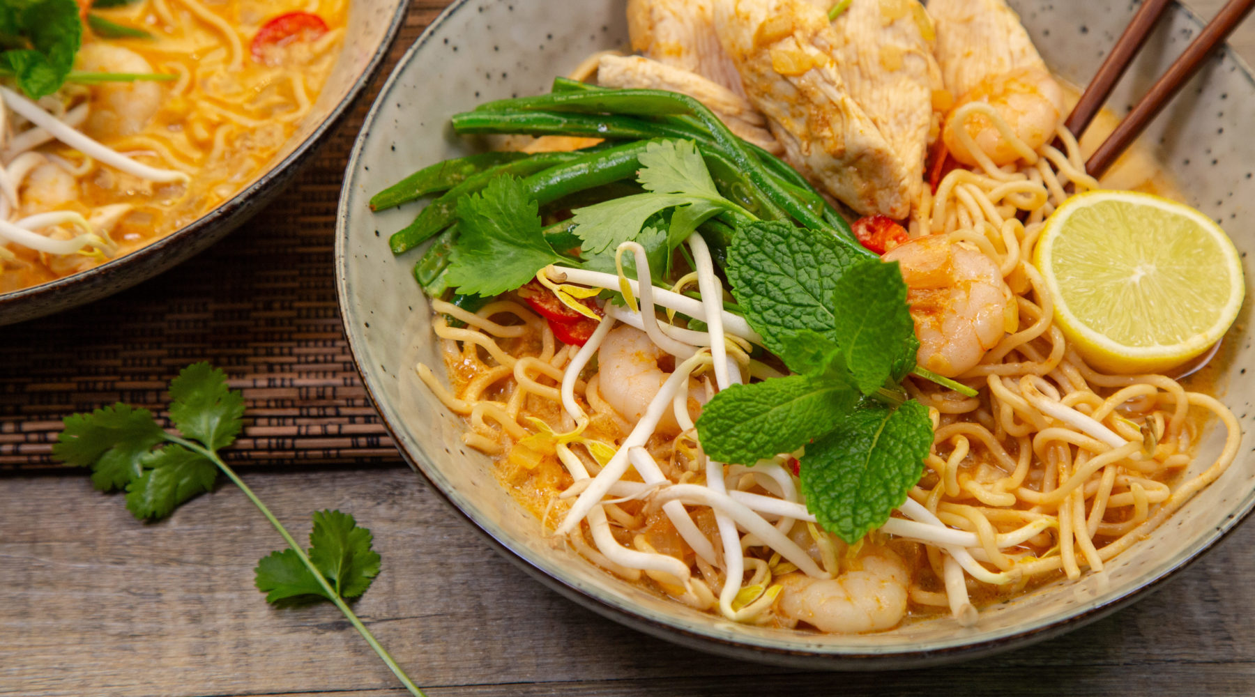 Two bols of noodle soup topped with chicken, prawn bean sprouts and herb.
