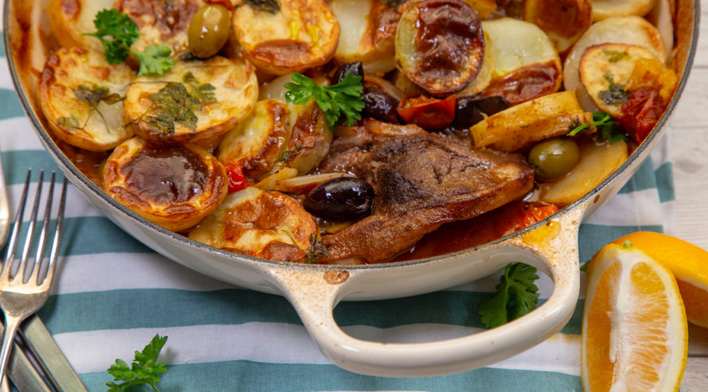 A casserole dish full of baked food, lemon wedges and forks.