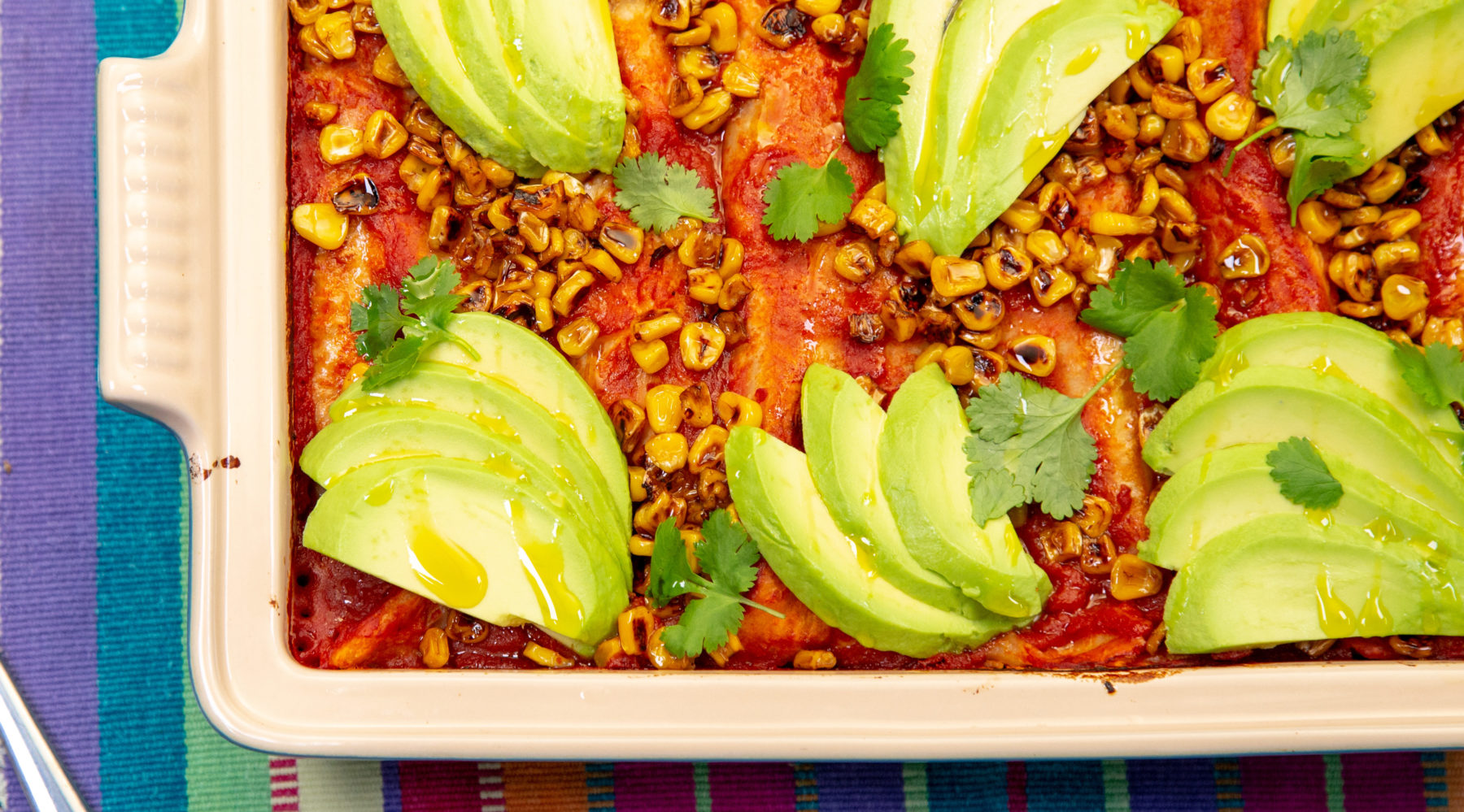 A rectangle oven dish full of red food topped with avocado slices.