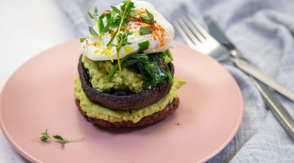 A mushroom and green mash stack topped with poached egg and herbs on a pink plate.