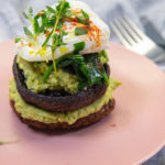 A mushroom and green mash stack topped with poached egg and herbs on a pink plate.