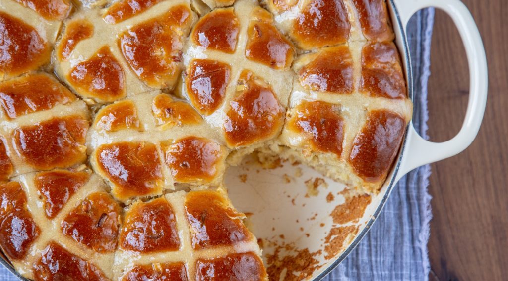 White cast iron pan full of hot cross buns,one small part of the bun torn out.