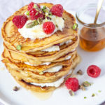 Pancakes stack with white cream and raspberries, and a jar of syrup.