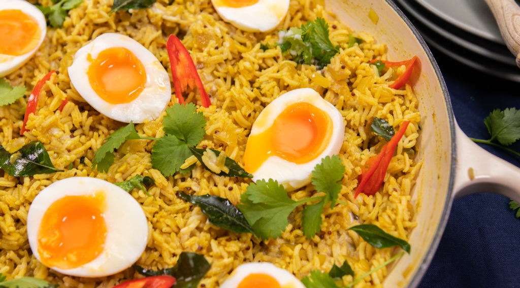 A white caserole dish full of yellow rice topped with boiled eggs and herbs.