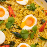 A white caserole dish full of yellow rice topped with boiled eggs and herbs.