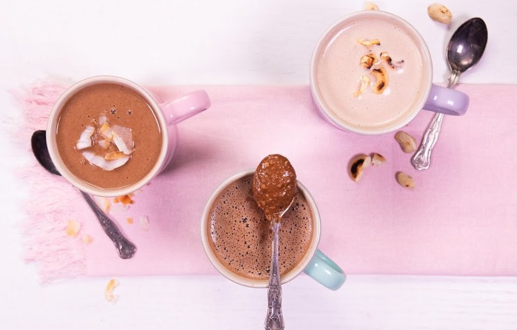 3 mugs of hot chocolate with spoons on pink background