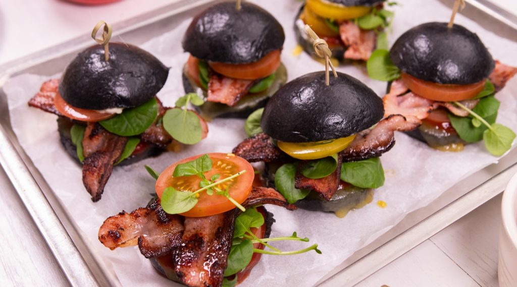 6 small black round bun sandwiches with skewers on a paper lined tray