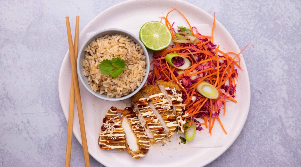 Chicken katsu served with brown rice and colourful salad on a plate