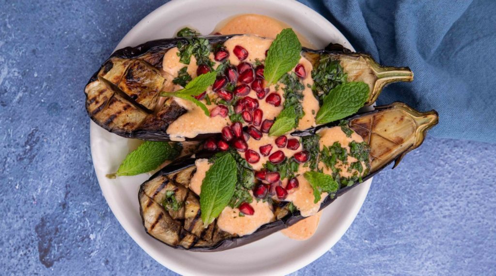 2 aubergine halves topped with pink sauce, herbs and red berries