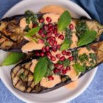 2 aubergine halves topped with pink sauce, herbs and red berries