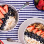 2 round bowls with strawberries and blueberries on blue and white striped cloth