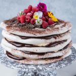 chocolate cream sandwiched layer cake with raspberries and flowers on top