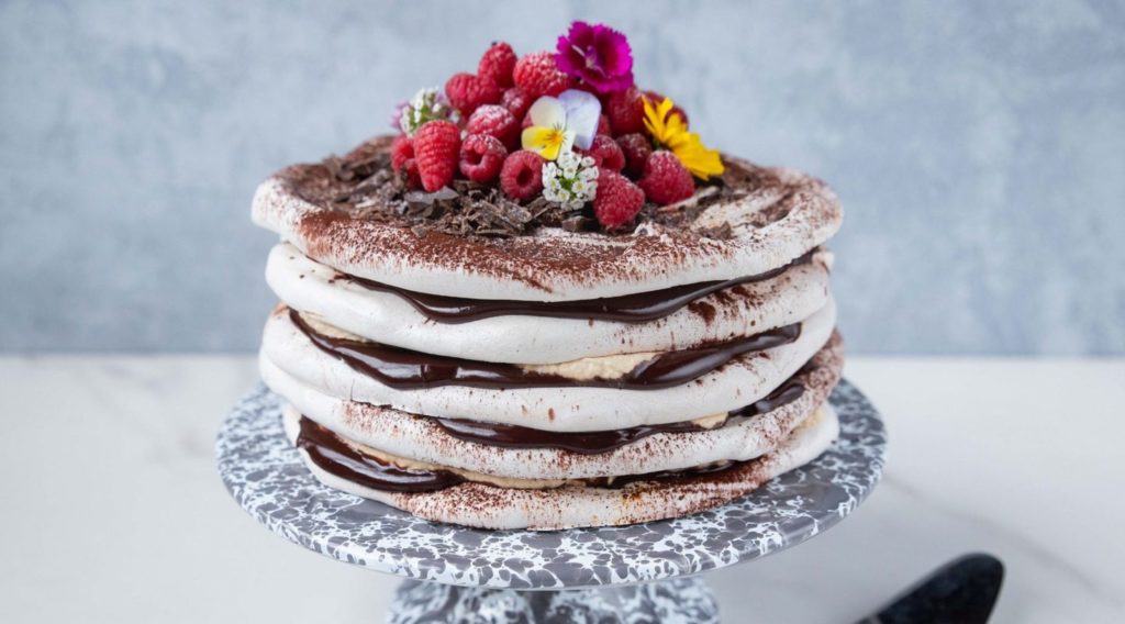 chocolate cream sandwiched layer cake with raspberries and flowers on top