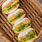 4 bao buns filled with fish nuggets on a bamboo steamer