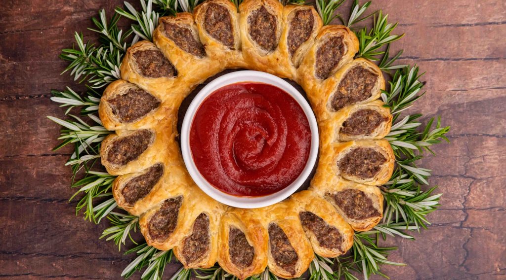 Red sauce in a pot surrounded by sausage rolls and greens