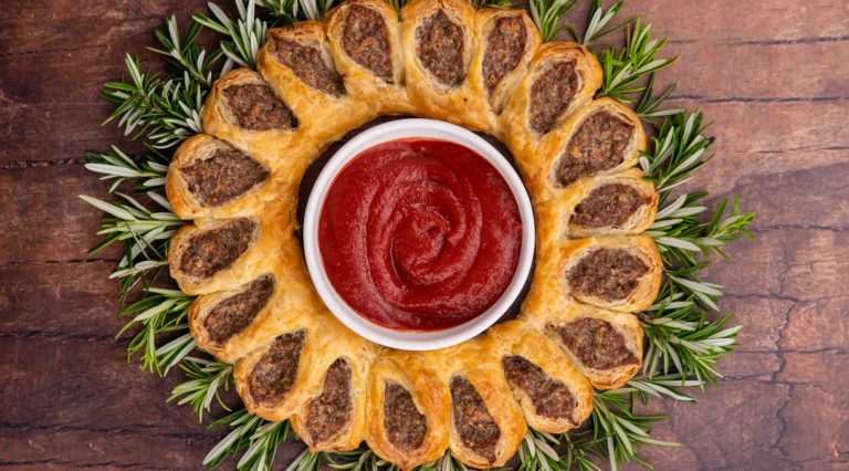 Red sauce in a pot surrounded by sausage rolls and greens