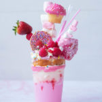 Pink milkshake in tall glass with lots of sweet pink toppings.