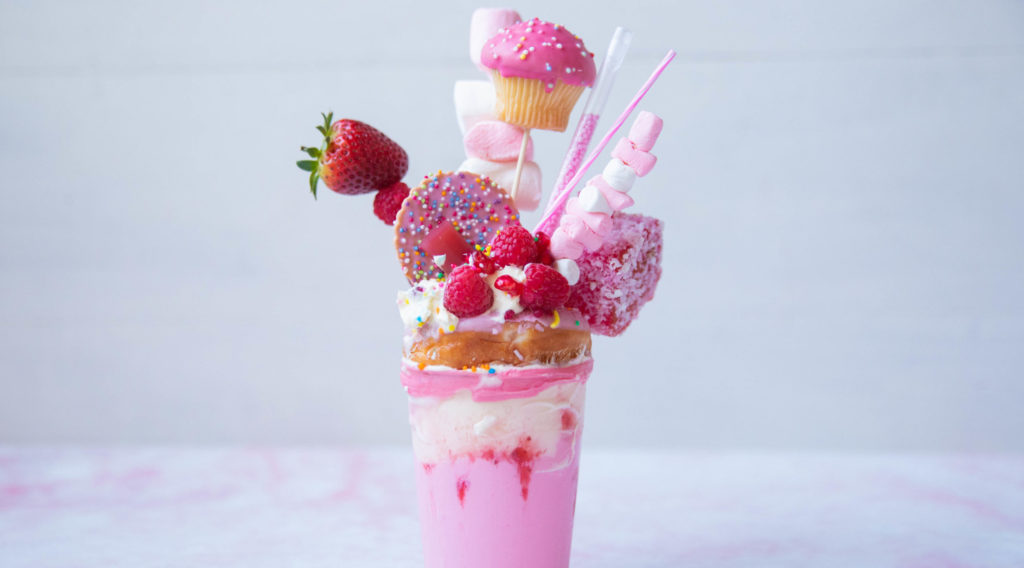 Pink milkshake in tall glass with lots of sweet pink toppings.