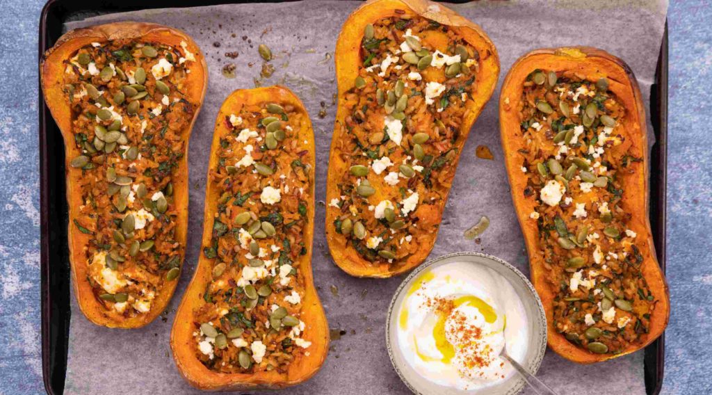 4 stuffed butternut squash halves on a baking tray with a pot of aioli