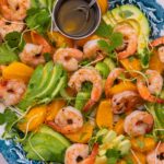 Prawns , Avocado slices, orange segments mixed on a blue oval plate on marble top.