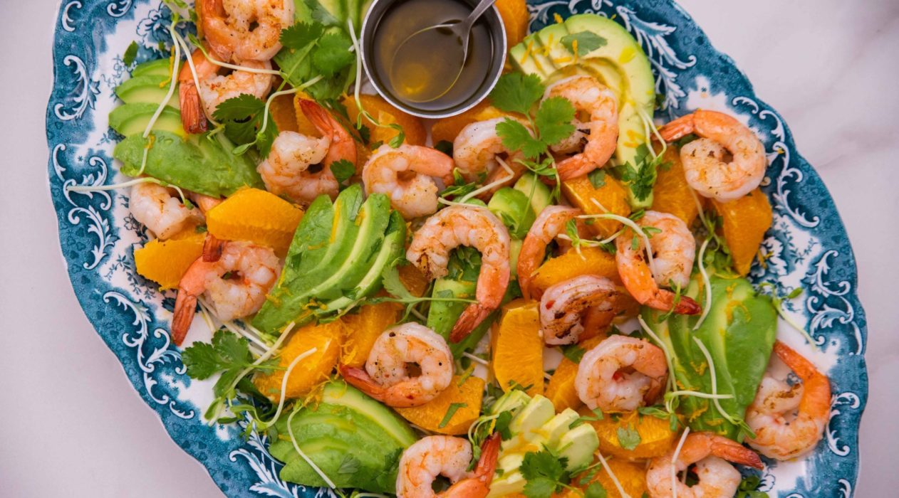 Prawns , Avocado slices, orange segments mixed on a blue oval plate on marble top.