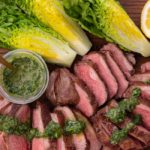 Meat slices and lettuce pieces on a wooden board with half lemon and a pot of green sauce
