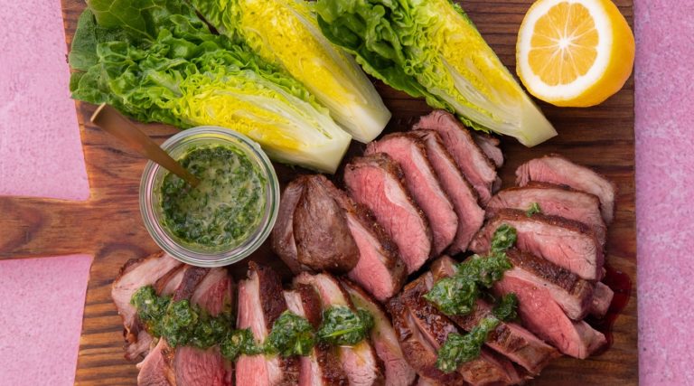 Meat slices and lettuce pieces on a wooden board with half lemon and a pot of green sauce