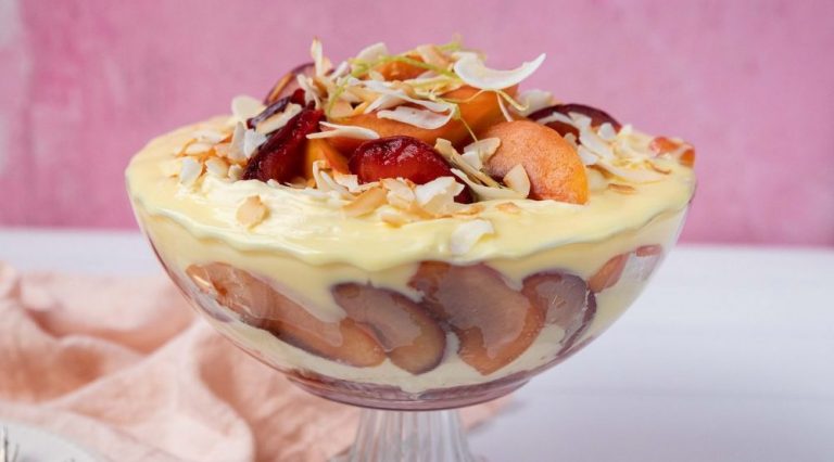 A glass bowl full of yellow cream and red and orange coloured fruit on pink & white background