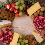 cheese, crackers and fruits placed in a ring on a wooden board