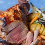 Lamb roast on bone with roasted potato and vegetables on a wooden board on blue background