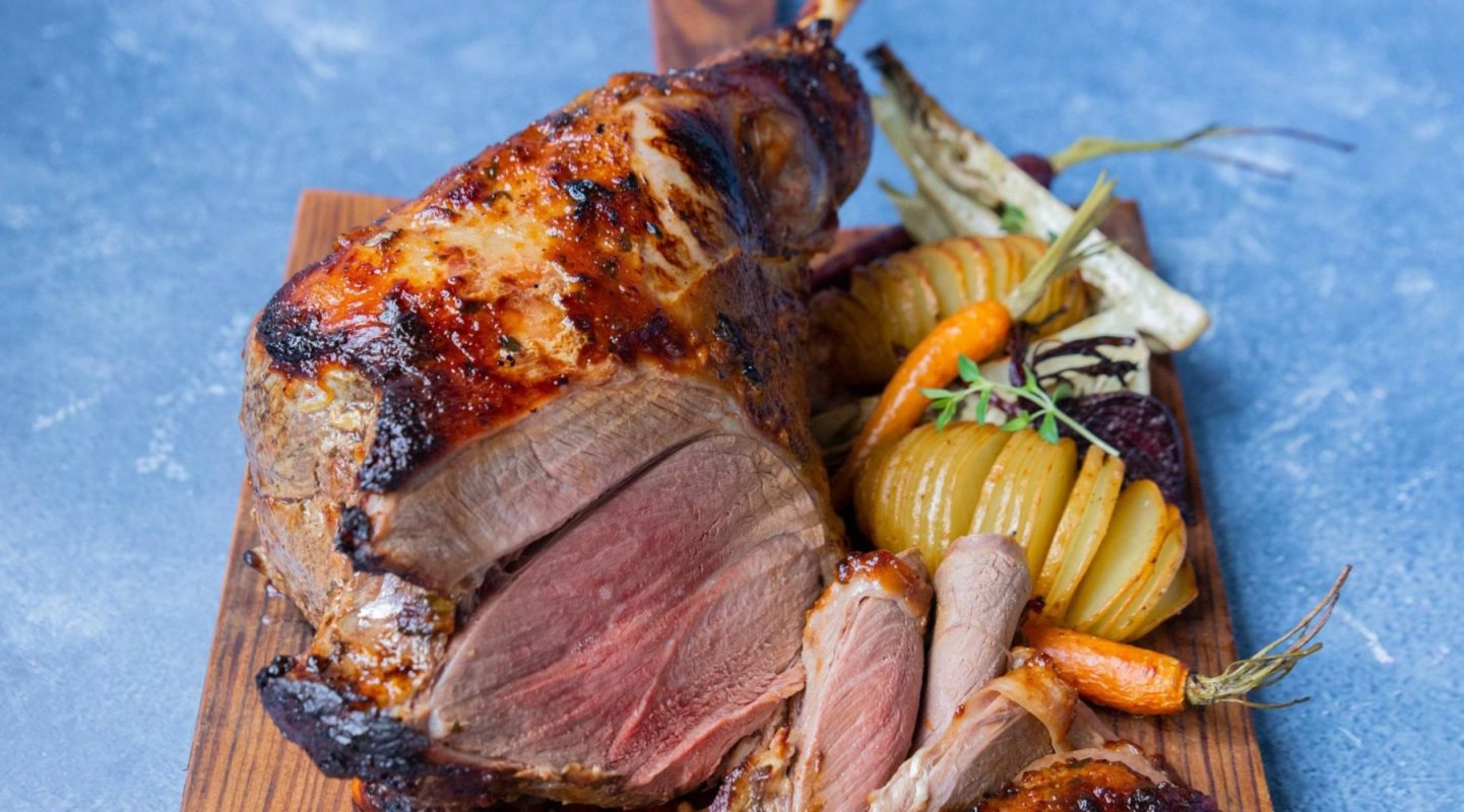 Lamb roast on bone with roasted potato and vegetables on a wooden board on blue background