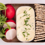 3 radishes, an oblong box full of cream topped with herbs and crackers in an oblong lunch box.
