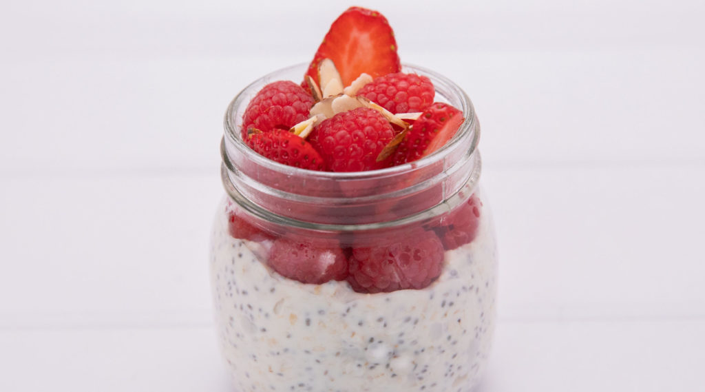 A clear glass jar filled with white yoghurt topped with red berries.