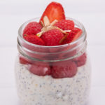 A clear glass jar filled with white yoghurt topped with red berries.