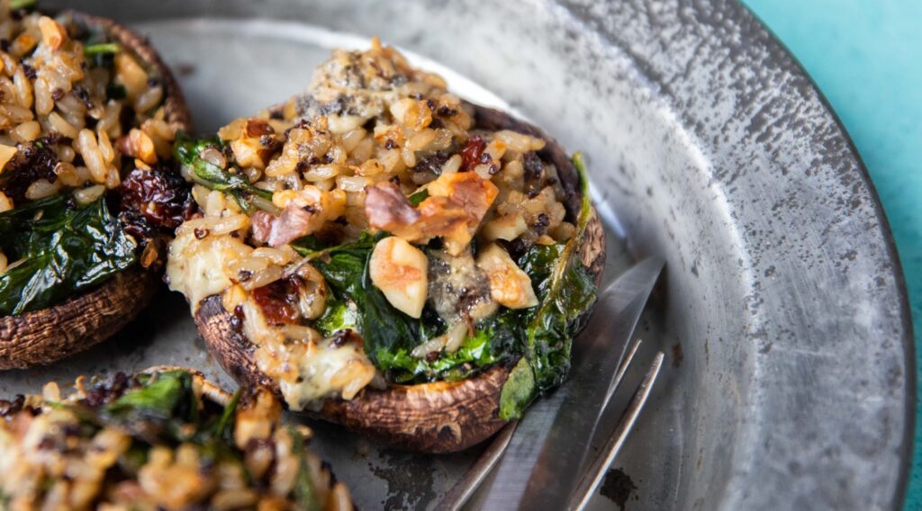 3 large mushrooms stuffed with greens and nuts on a metal plate with a knife and fork.