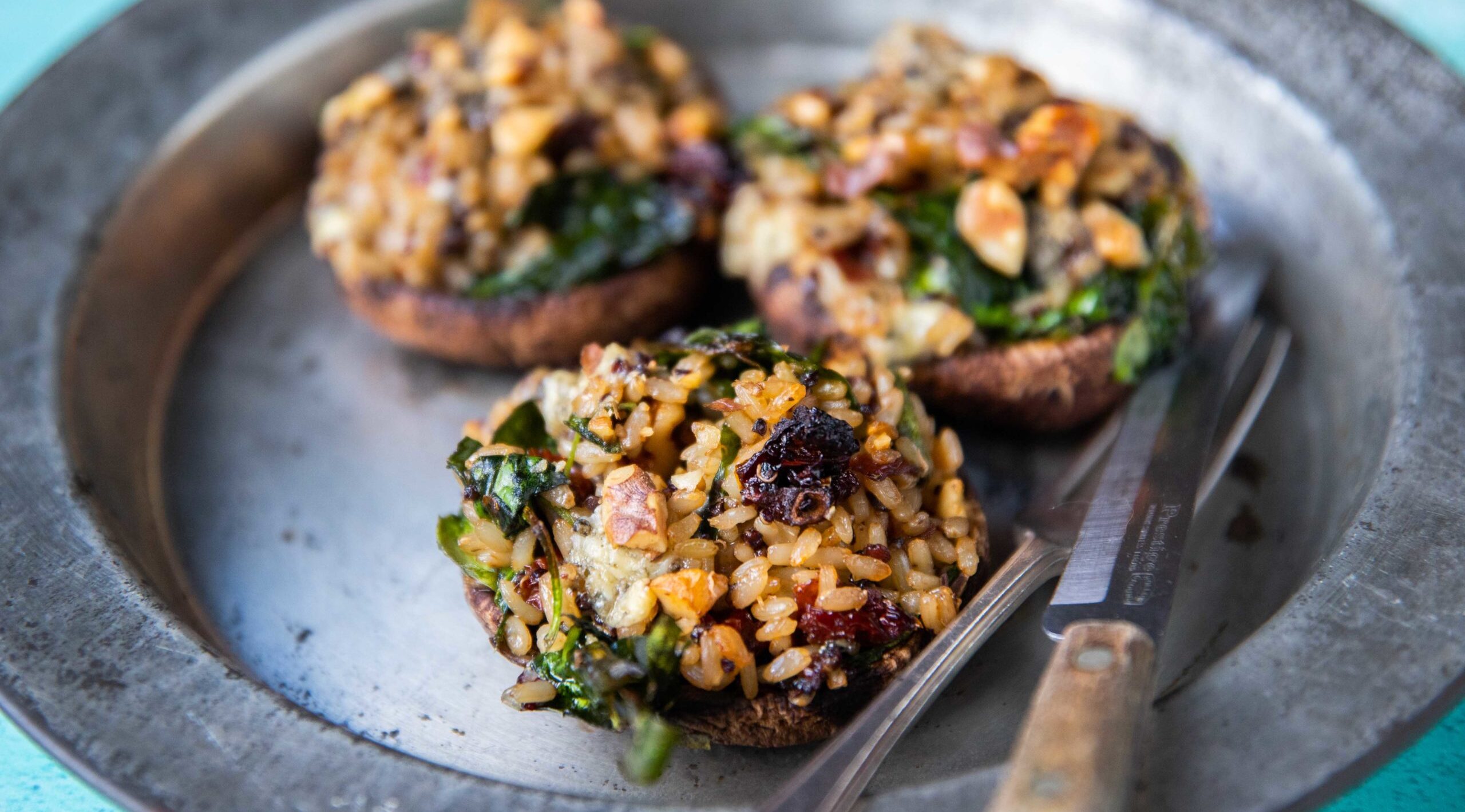 3 large mushrooms stuffed with rice,greens and nuts on a metal plate with knife and fork.