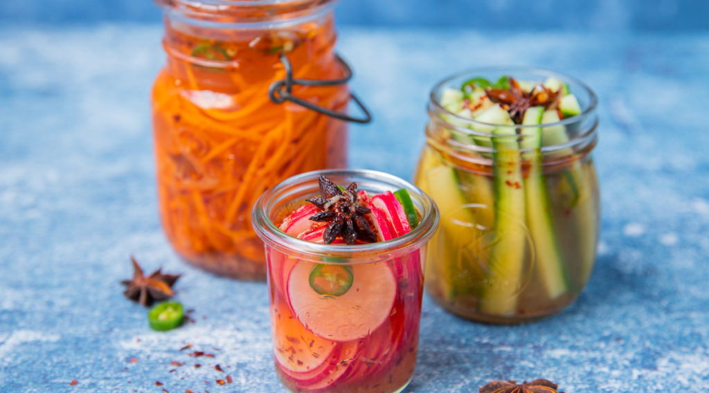 3 jars of pickled vegetables, carrot, cucumber and radish on blue paper
