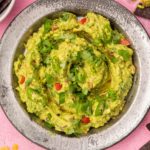 Plate of chunky guacamole with chili, coriander and corn chips on pink background